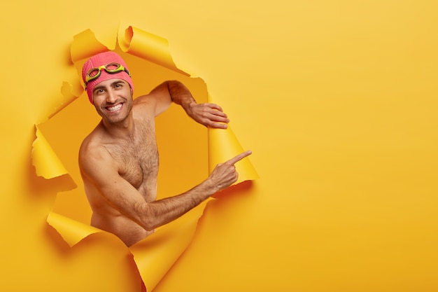 Hombre guapo alegre recrea durante las vacaciones de verano, hace fotos creativas, posa en un agujero de papel rasgado