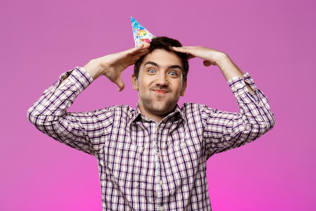 Hombre guapo alegre sonriendo, regocijándose sobre la pared púrpura. Fiesta de cumpleaños.