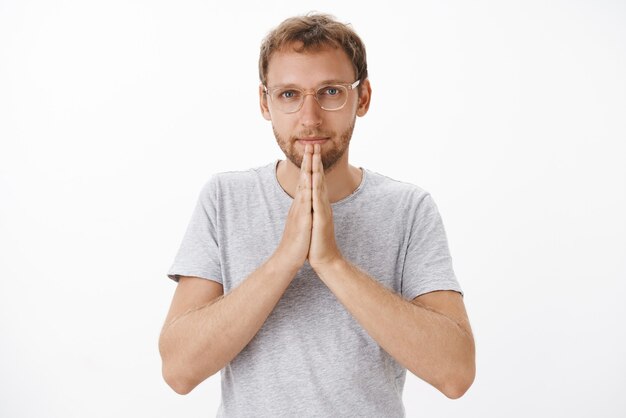 Hombre guapo y amable agradecido con cerdas en vasos y camiseta gris casual tomados de la mano en oración