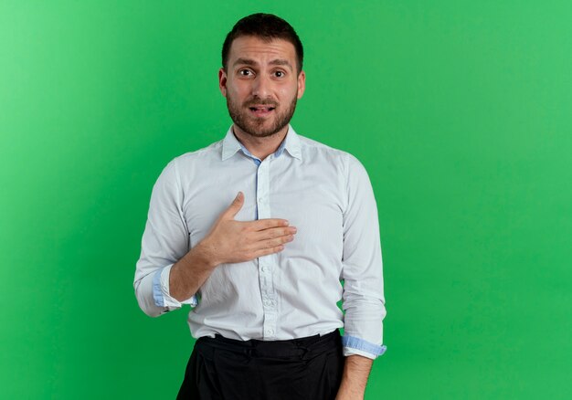 Hombre guapo ansioso pone la mano en la barbilla aislada en la pared verde