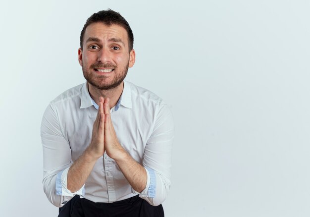 Hombre guapo ansioso toma las manos juntas mirando aislado en la pared blanca