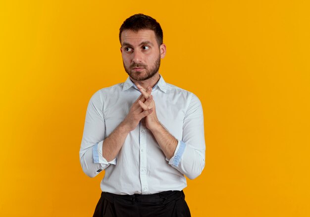 Hombre guapo ansioso toma las manos juntas mirando al lado aislado en la pared naranja