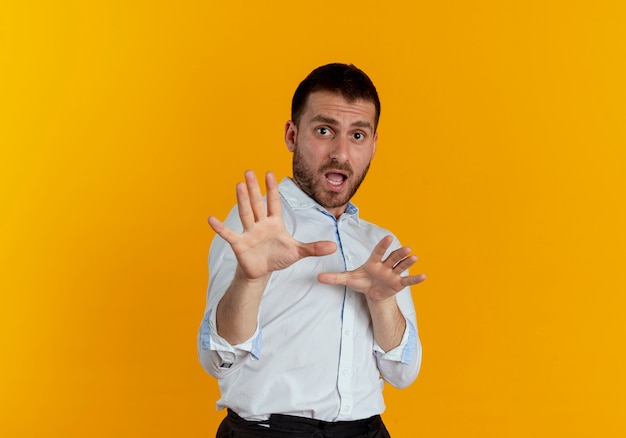 Hombre guapo asustado finge defender con las manos aisladas en la pared naranja