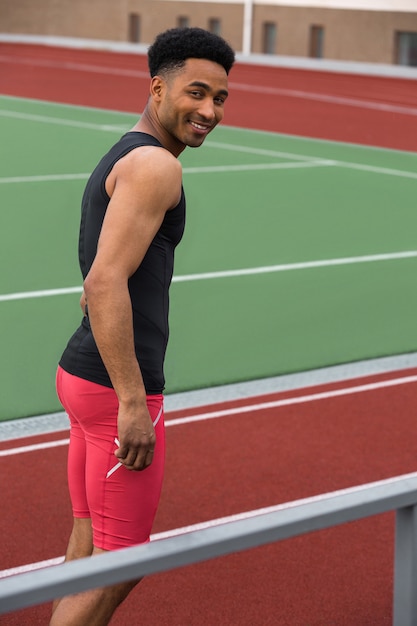 Hombre guapo atleta africano sonriente en la pista de atletismo