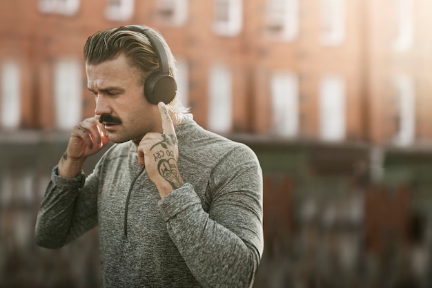 Hombre guapo con auriculares inalámbricos en los medios de comunicación remezclados de la ciudad