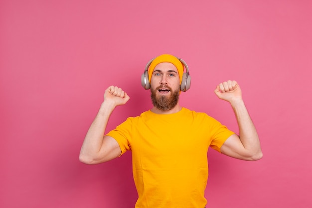 Hombre guapo en baile casual con auriculares aislados sobre fondo rosa