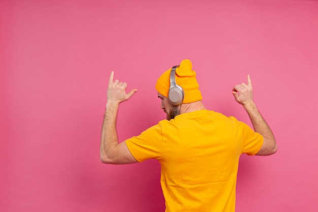 Hombre guapo en baile casual con auriculares aislados sobre fondo rosa