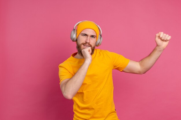 Hombre guapo en baile casual con auriculares aislados sobre fondo rosa