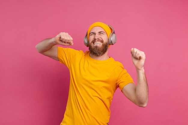 Hombre guapo en baile casual con auriculares aislados sobre fondo rosa