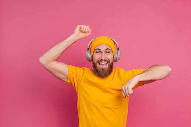 Hombre guapo en baile casual con auriculares aislados sobre fondo rosa