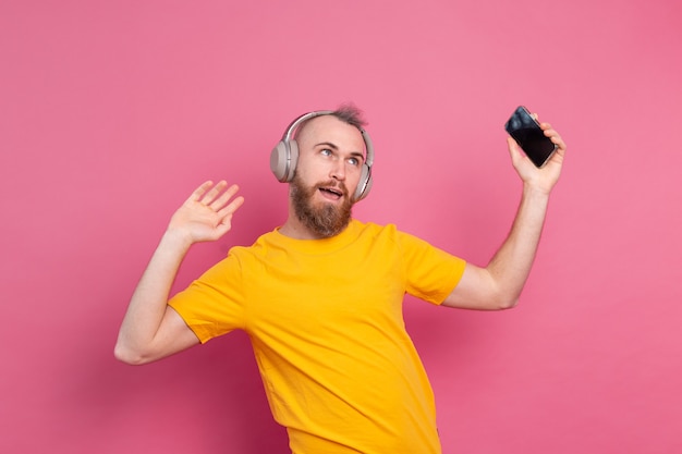 Hombre guapo en baile casual con teléfono móvil y auriculares aislados sobre fondo rosa