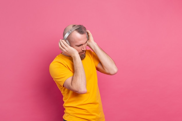 Hombre guapo en baile casual con teléfono móvil y auriculares aislados sobre fondo rosa