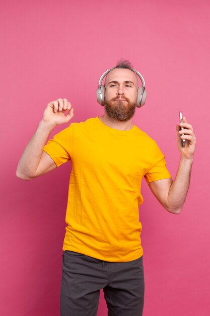 Hombre guapo en baile casual con teléfono móvil y auriculares aislados sobre fondo rosa