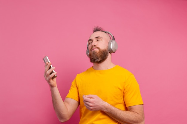 Hombre guapo en baile casual con teléfono móvil y auriculares aislados sobre fondo rosa