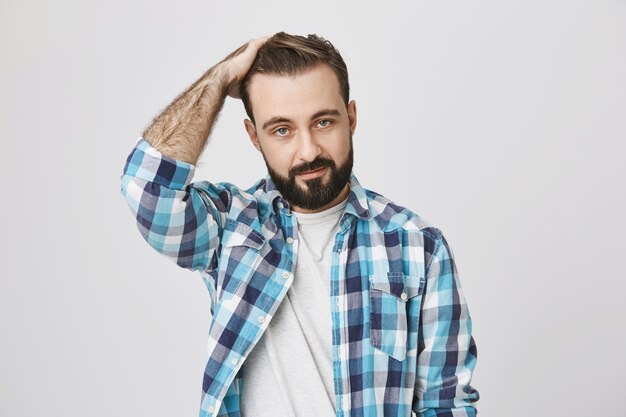 Hombre guapo con barba corre de la mano por el cabello y se ve descarado