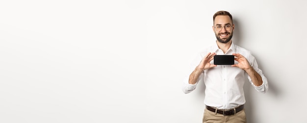 Foto gratuita hombre guapo con barba en gafas que demuestra la aplicación de teléfono móvil que muestra la pantalla del teléfono inteligente sta