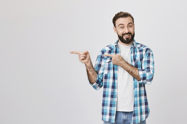 Hombre guapo con barba sonriente apuntando a la izquierda