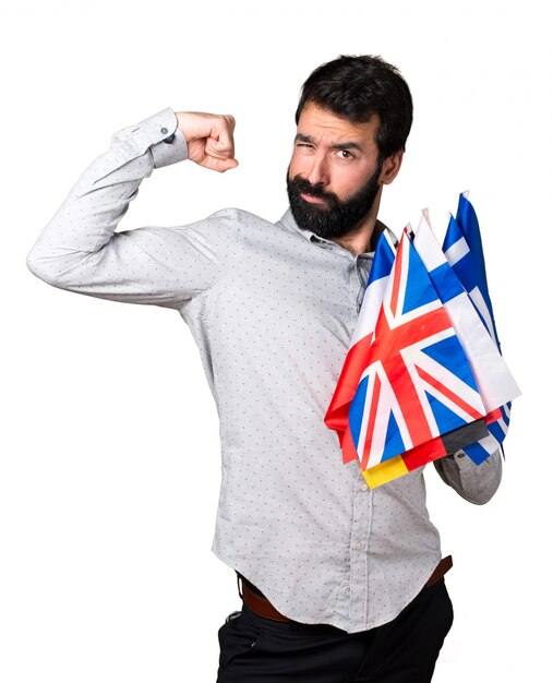 Hombre guapo con barba sosteniendo muchas banderas y haciendo gesto fuerte