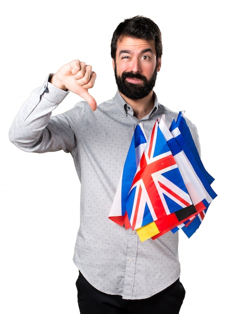 Hombre guapo con barba sosteniendo muchas banderas y haciendo mala señal