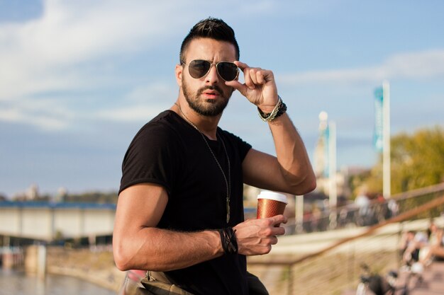 Hombre guapo beber café al aire libre. Con gafas de sol, un tipo con barba. Efecto Instagram.