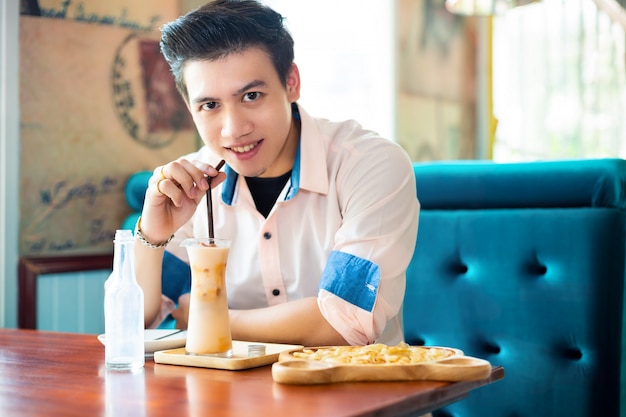 Hombre guapo beber té helado en la cafetería