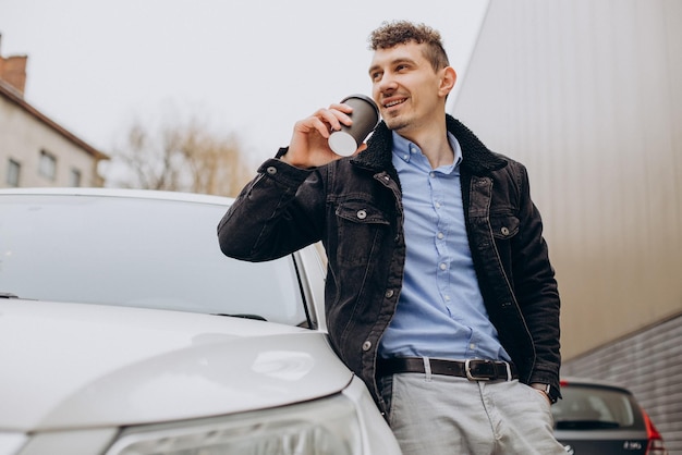 Hombre guapo bebiendo café junto a su auto