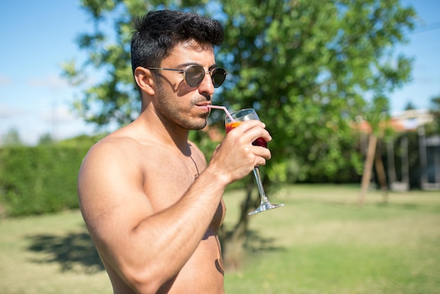 Hombre guapo bebiendo cócteles brillantes. Hombre con gafas de sol con vaso con bebida brillante. Ocio, amistad, concepto de fiesta