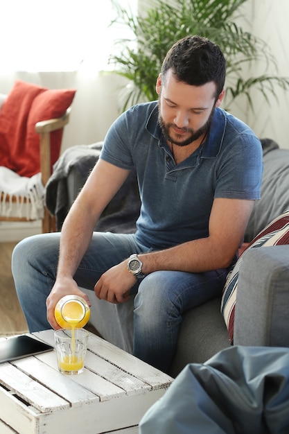 Hombre guapo bebiendo jugo de naranja en el sofá