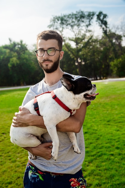 Foto gratuita hombre guapo con bulldog francés, caminando en el parque