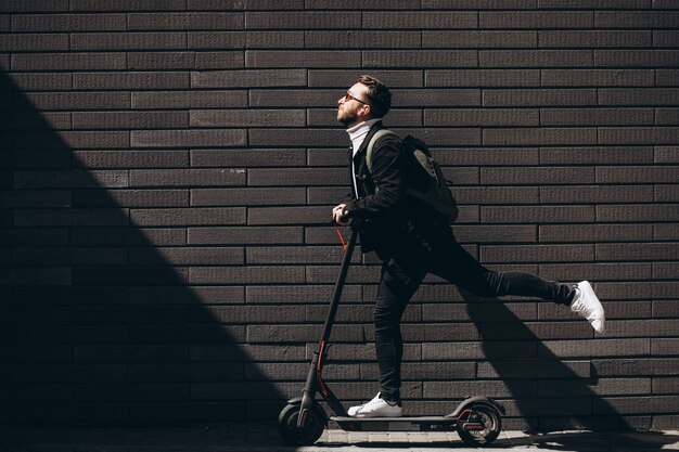 Hombre guapo cabalgando en la ciudad en scooter