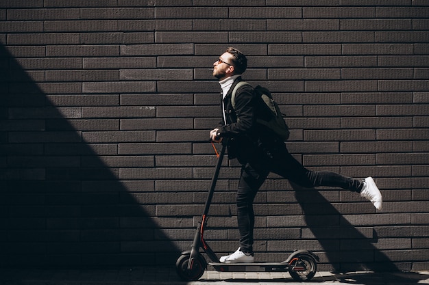 Hombre guapo cabalgando en la ciudad en scooter