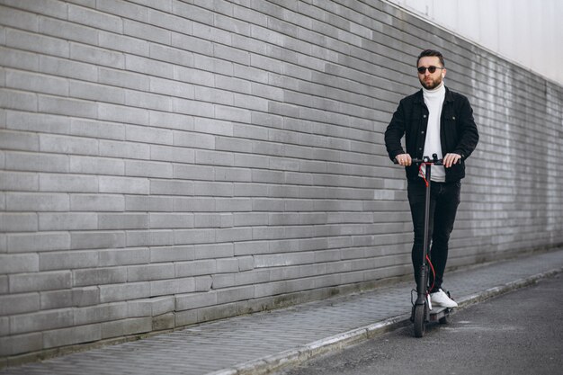 Hombre guapo cabalgando en la ciudad en scooter