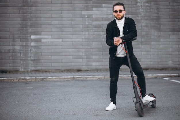 Hombre guapo cabalgando en la ciudad en scooter