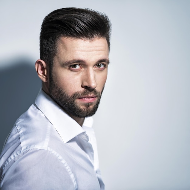 Foto gratuita hombre guapo con camisa blanca, posando. chico atractivo con peinado de moda. hombre confiado con barba corta. chico adulto con cabello castaño. retrato de primer plano.