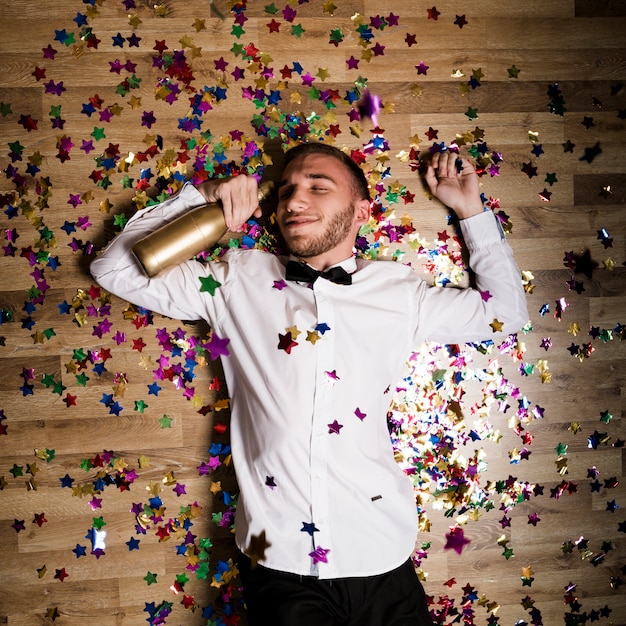 Hombre guapo en camisa con botella de bebida entre confeti