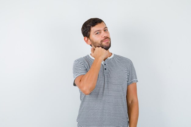 Hombre guapo en camiseta manteniendo el puño debajo de la barbilla y mirando confiado, vista frontal.