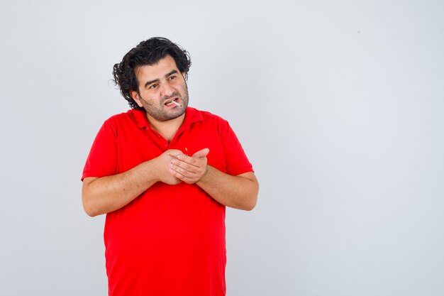 Hombre guapo en camiseta roja sosteniendo el encendedor de cigarrillos en las manos, de pie con el cigarrillo en la boca y mirando serio, vista frontal.