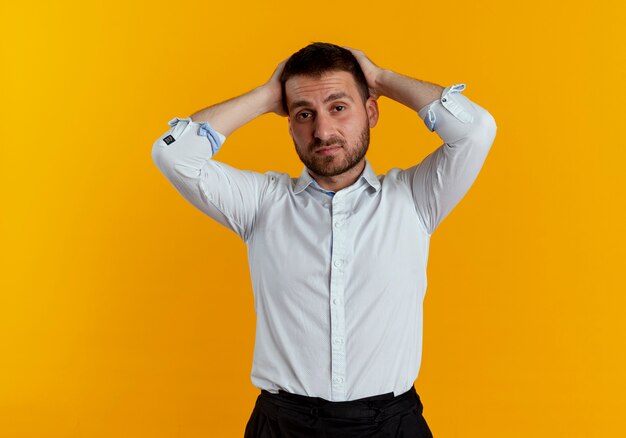 Hombre guapo cansado sostiene la cabeza con las dos manos aisladas en la pared naranja