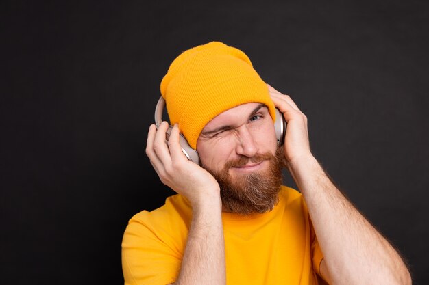 Hombre guapo en casual escuchando música con auriculares aislado sobre fondo negro