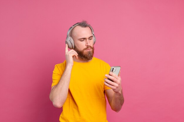 Hombre guapo en casual escuchando música con auriculares aislado sobre fondo rosa