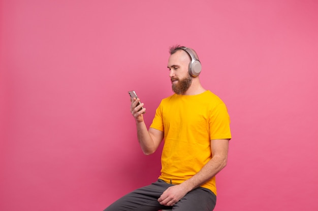 Hombre guapo en casual escuchando música con auriculares aislado sobre fondo rosa