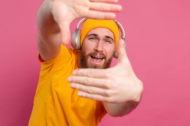 Hombre guapo en casual escuchando música con auriculares aislado sobre fondo rosa