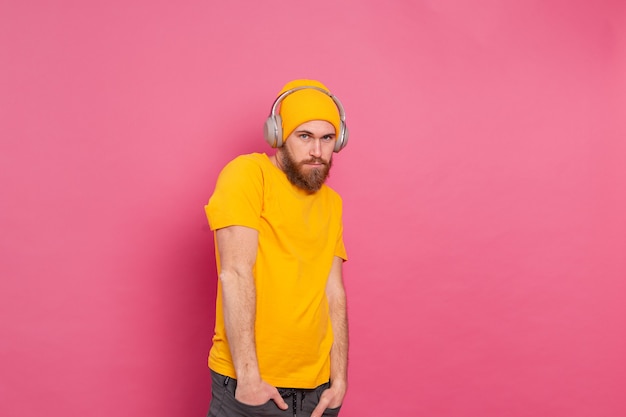 Foto gratuita hombre guapo en casual escuchando música con auriculares aislado sobre fondo rosa