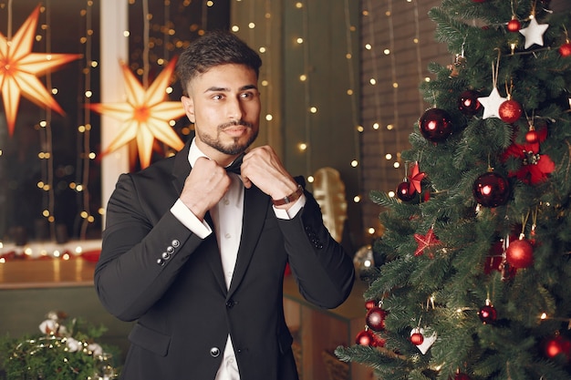 Hombre guapo cerca del árbol de Navidad. Gentelman con traje negro.