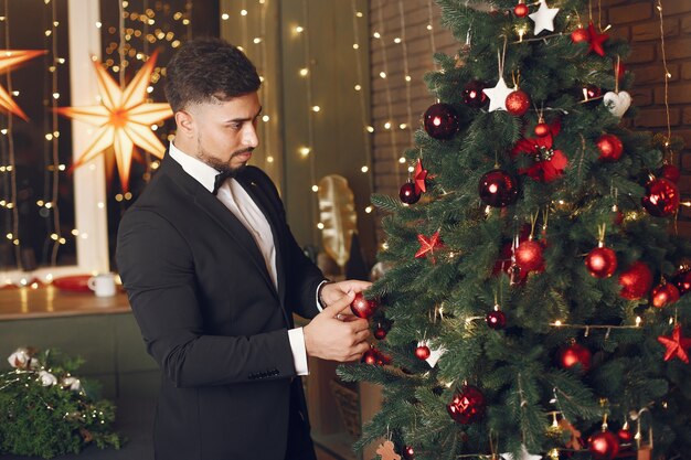 Hombre guapo cerca del árbol de Navidad. Gentelman con traje negro.