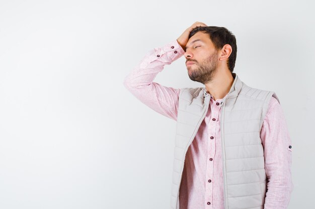 Hombre guapo con chaleco, camisa manteniendo la mano en la cabeza mientras cierra los ojos y parece cansado,