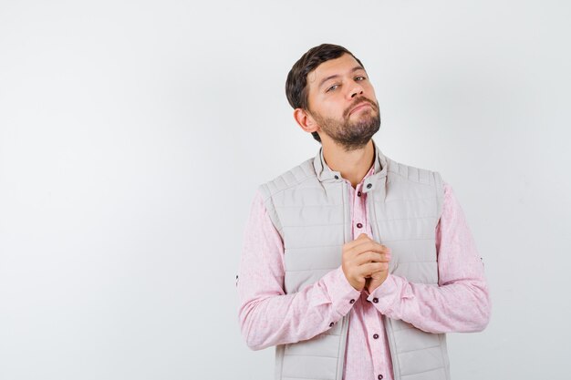 Hombre guapo en chaleco, camisa manteniendo las manos juntas y mirando confiado,