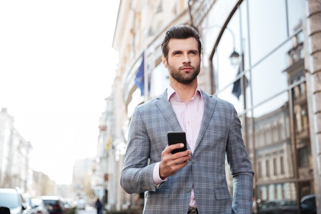 Hombre guapo en una chaqueta caminando y sosteniendo el teléfono móvil