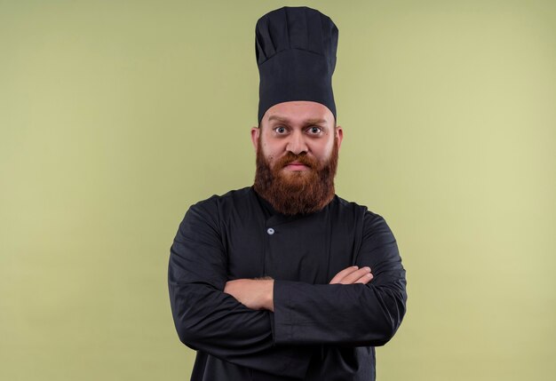 Un hombre guapo chef barbudo en uniforme negro tomados de la mano mientras mira en una pared verde