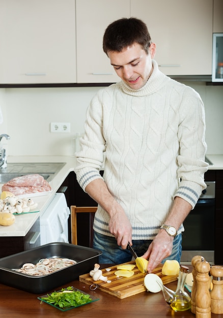 Hombre guapo cocinando carne con champiñones y patatas